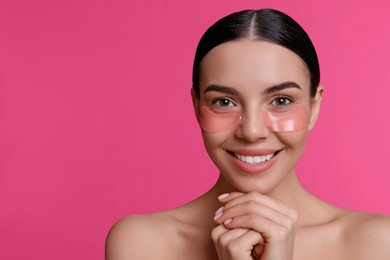 Beautiful young woman with under eye patches on pink background