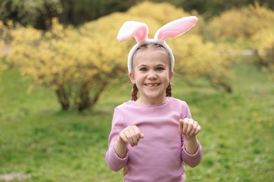 Easter celebration. Cute little girl with bunny ears outdoors, space for text