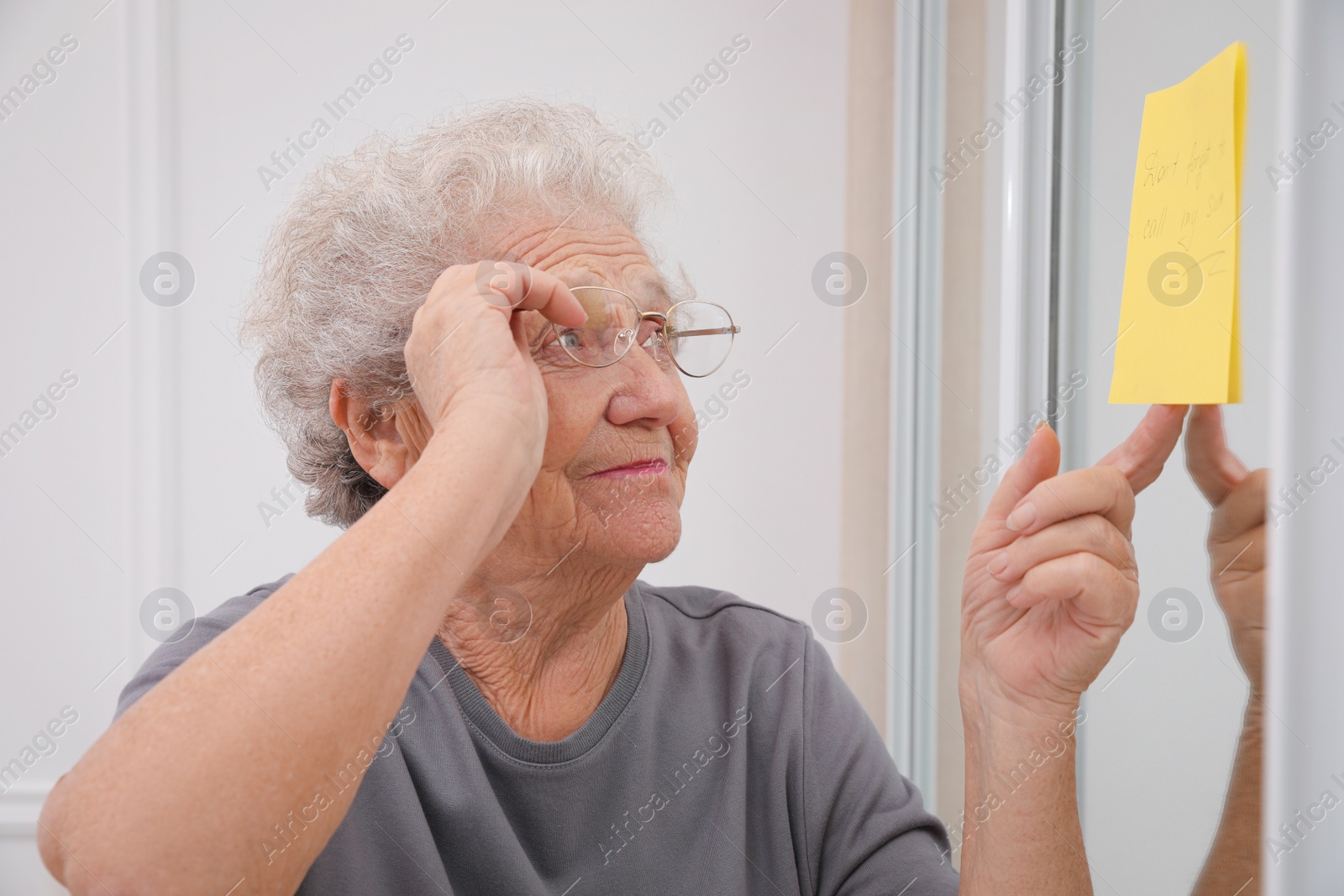 Photo of Senior woman looking at reminder note indoors. Age-related memory impairment