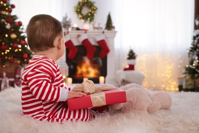Cute baby with gift box on floor in room decorated for Christmas