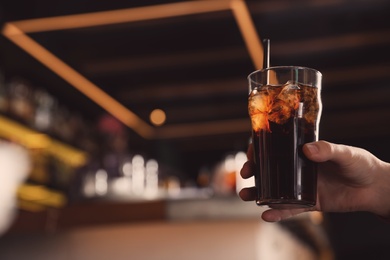 Man holding glass of refreshing cola indoors, closeup. Space for text