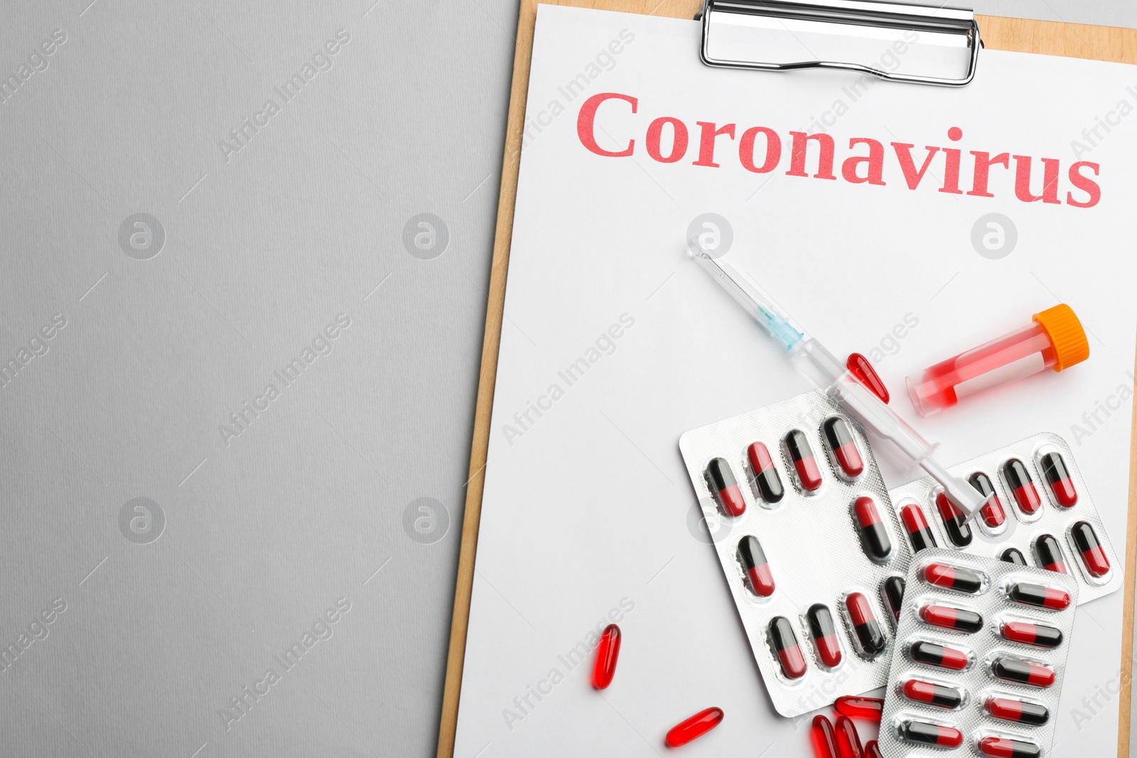 Photo of Clipboard with word CORONAVIRUS, test tube, syringe and medicine on light grey background, top view