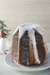 Photo of Delicious Pandoro cake decorated with powdered sugar on white wooden table. Traditional Italian pastry