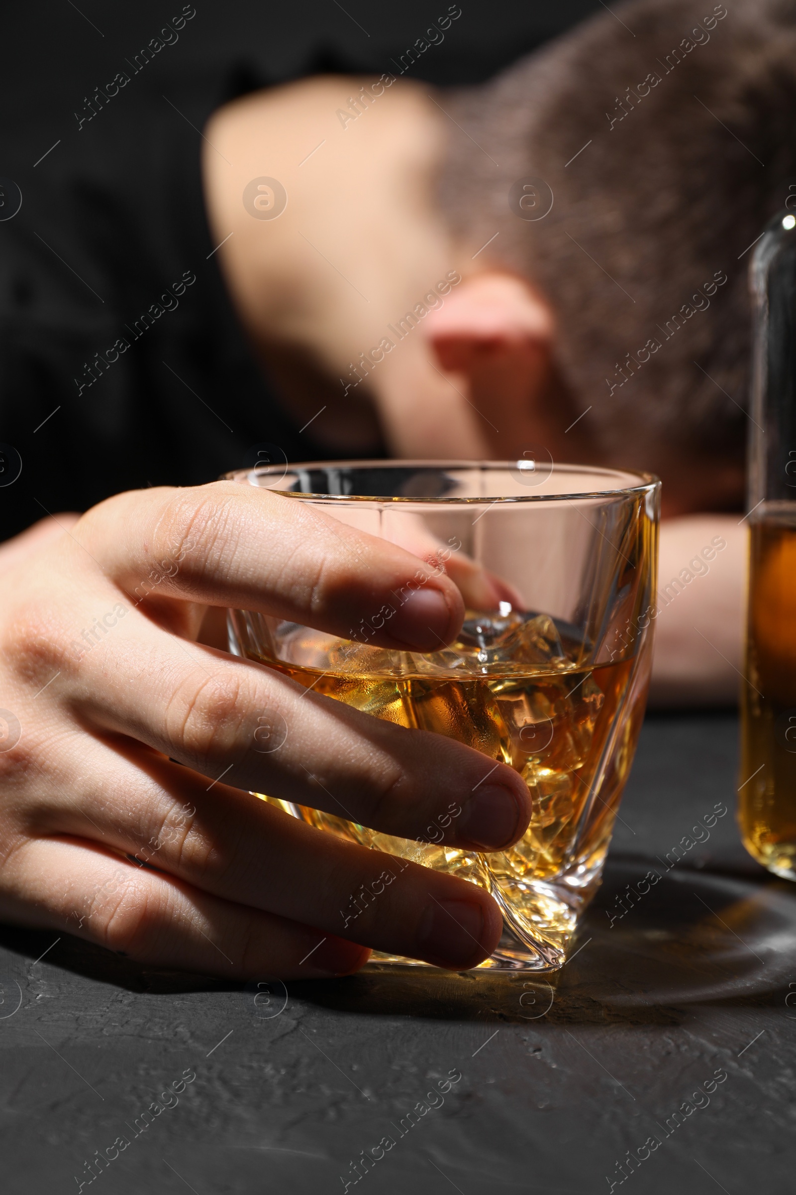 Photo of Alcohol addiction. Man with glass of whiskey at dark textured table, selective focus