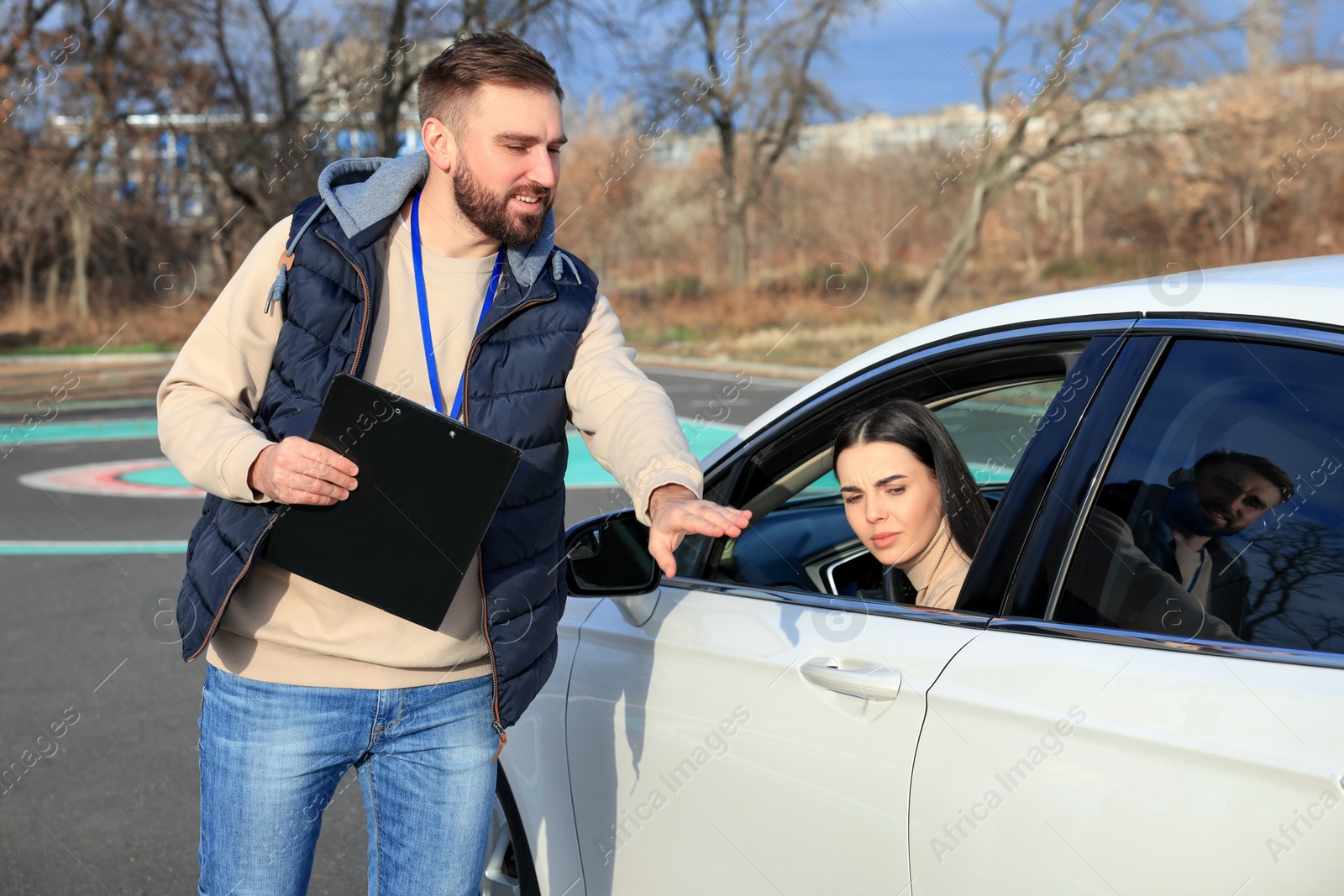 Photo of Instructor near car with young woman during exam on test track. Driving school