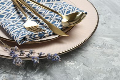 Clean plates, cutlery, napkin and lavender flowers on light grey textured table, closeup