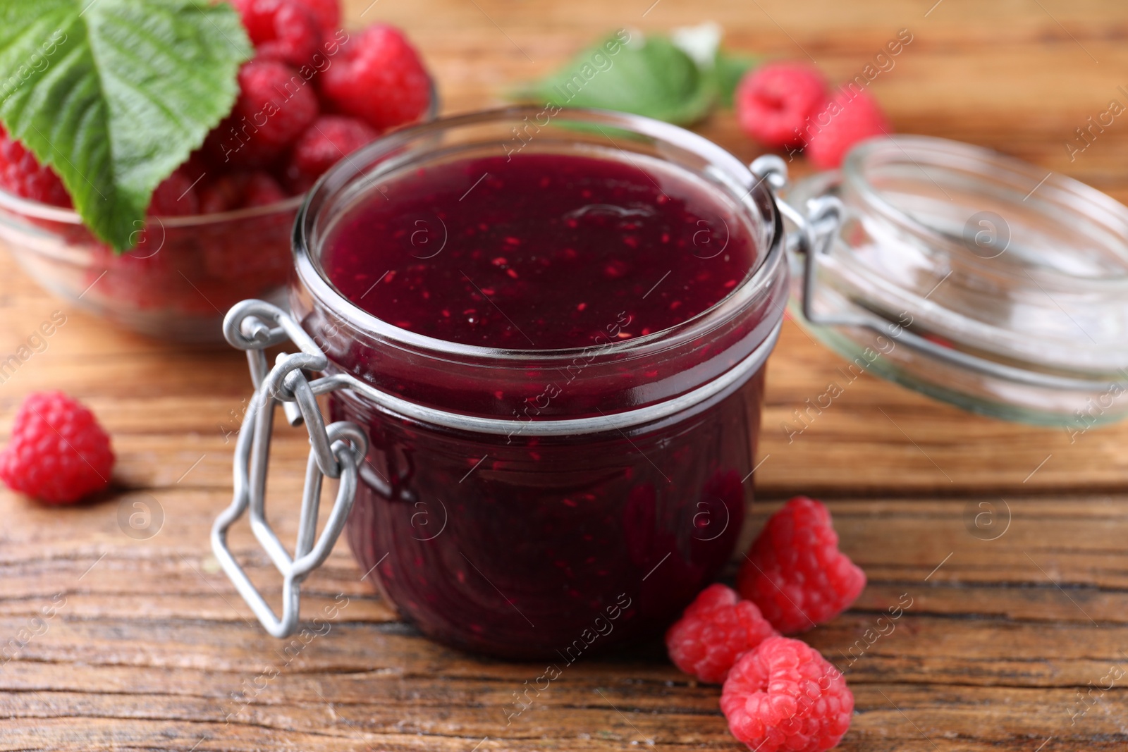 Photo of Jar of delicious raspberry jam and fresh berries on wooden table, closeup