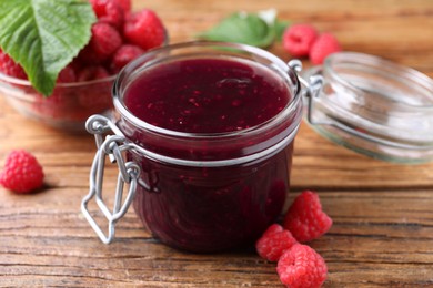 Jar of delicious raspberry jam and fresh berries on wooden table, closeup