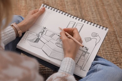 Woman sketching living room interior in notebook with pencil at home, closeup