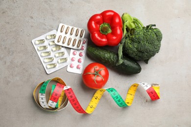 Photo of Weight loss pills, different vegetables and measuring tape on grey table, flat lay