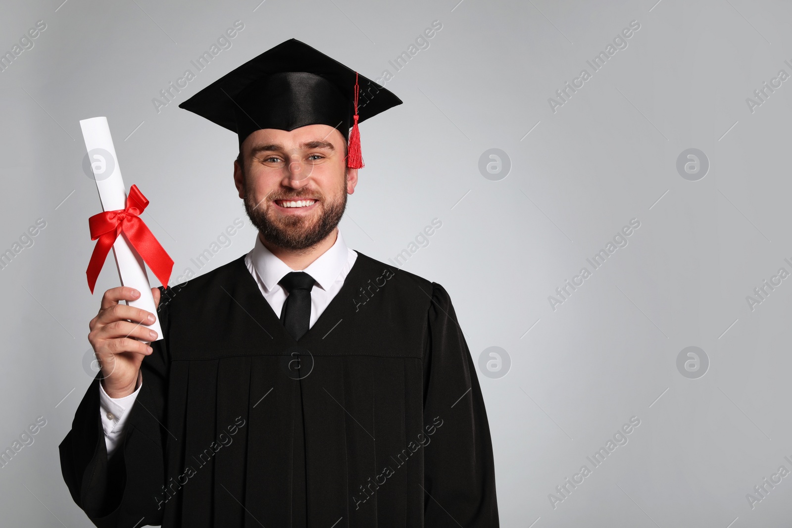 Photo of Happy student with graduation hat and diploma on grey background. Space for text