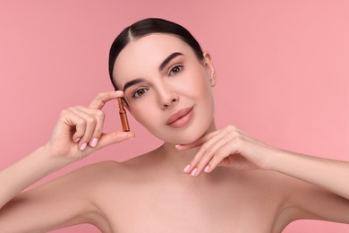 Photo of Beautiful young woman holding skincare ampoule on pink background