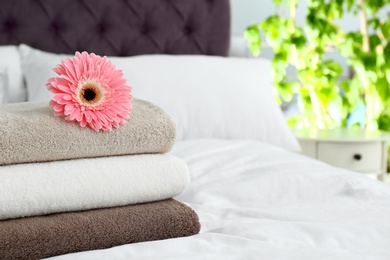 Photo of Stack of clean towels and beautiful gerbera flower on bed. Space for text