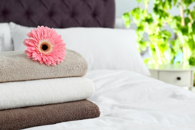 Stack of clean towels and beautiful gerbera flower on bed. Space for text