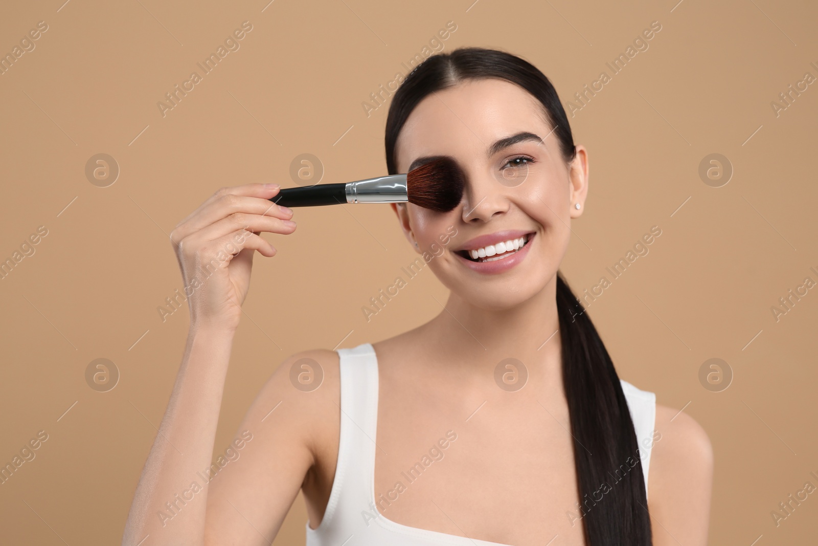 Photo of Beautiful woman with makeup brush on light brown background