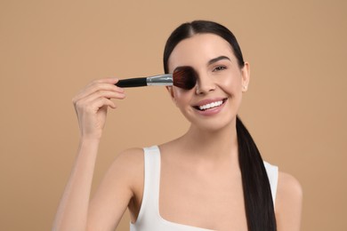 Beautiful woman with makeup brush on light brown background