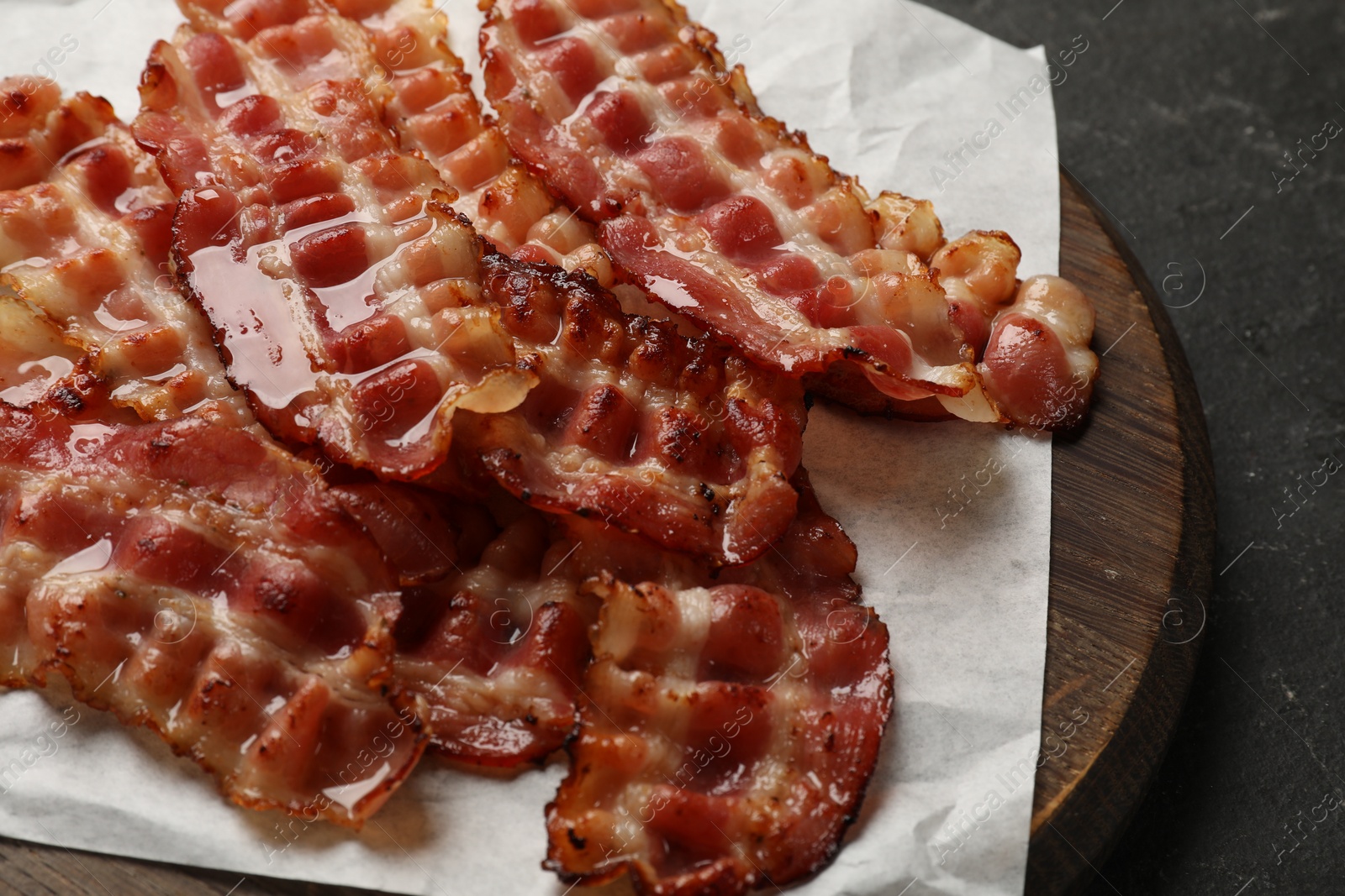 Photo of Board with fried bacon slices on dark table, closeup