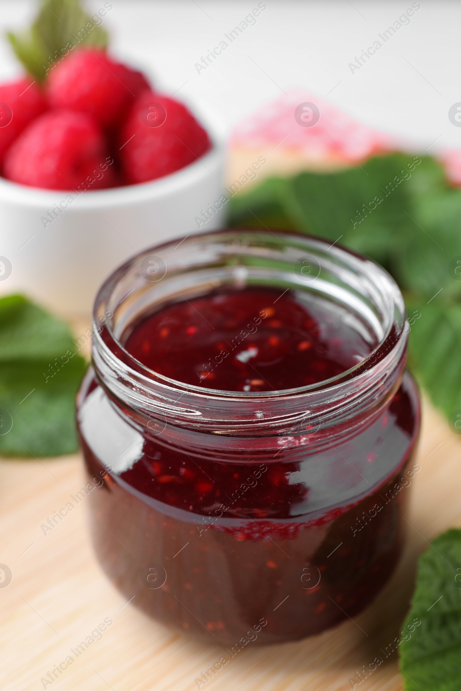 Photo of Jar of delicious raspberry jam on table, closeup