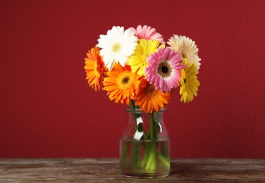 Photo of Bouquet of beautiful bright gerbera flowers in vase on wooden table against color background
