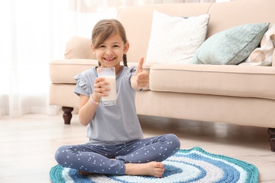 Photo of Cute little girl drinking milk on floor at home