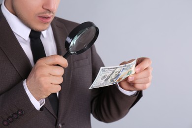 Photo of Expert authenticating 100 dollar banknote with magnifying glass on light grey background, closeup. Fake money concept