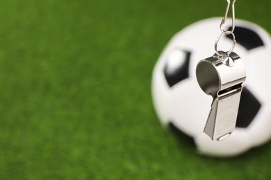 Photo of Football referee equipment. Metal whistle and soccer ball on green grass, closeup with space for text