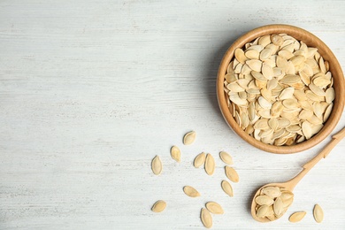 Photo of Raw unpeeled pumpkin seeds on white wooden table, flat lay. Space for text