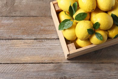 Fresh lemons and green leaves in crate on wooden table, top view. Space for text