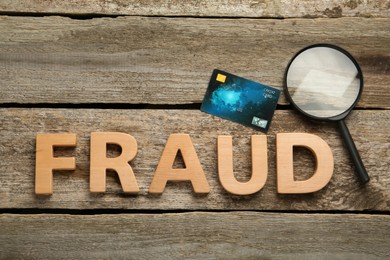 Photo of Word Fraud, credit card and magnifying glass on wooden background, flat lay