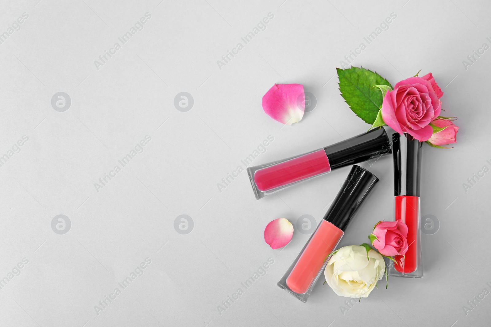 Photo of Lip glosses and flowers on light background