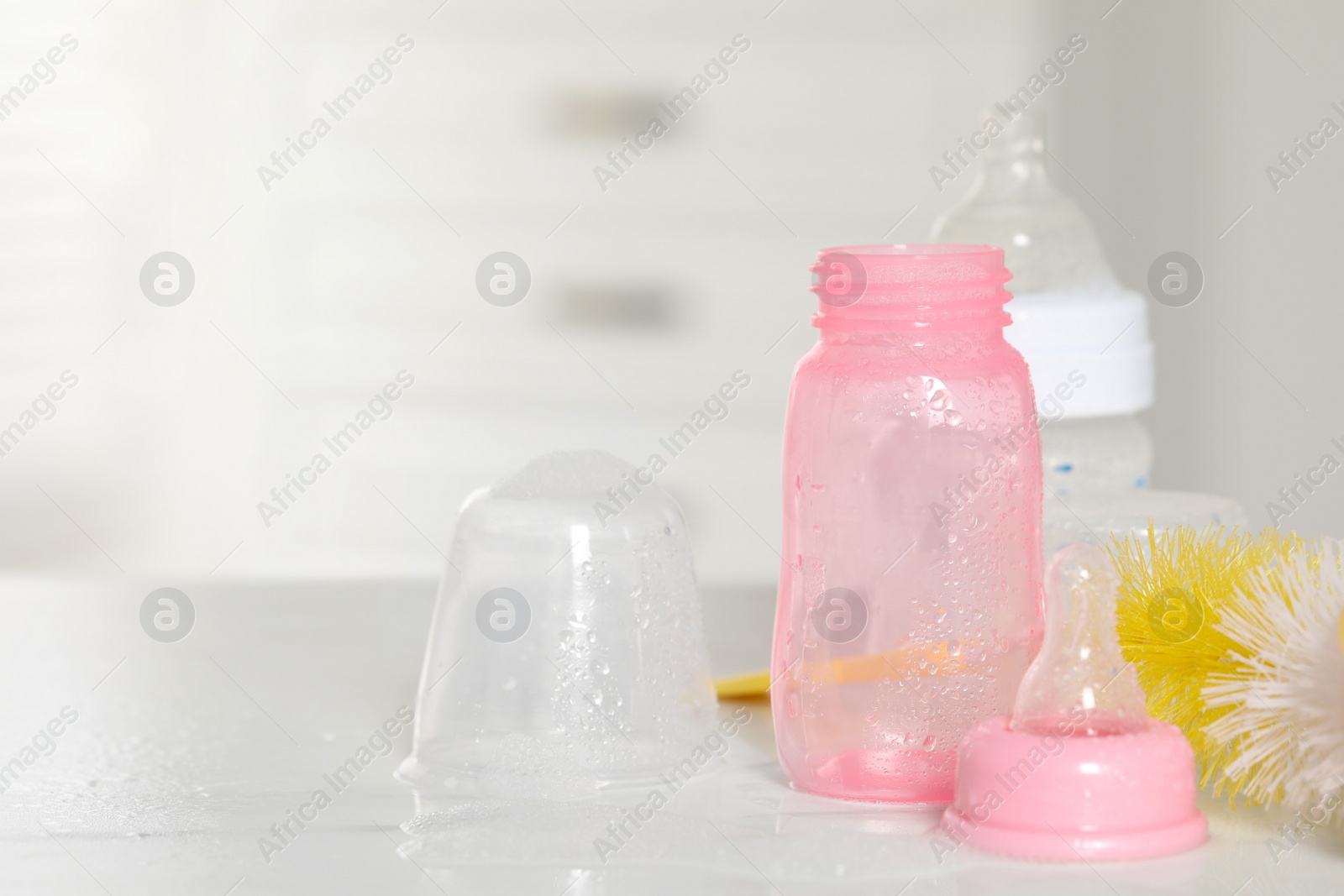 Photo of Clean baby bottles with nipples after sterilization and cleaning brush on white table indoors