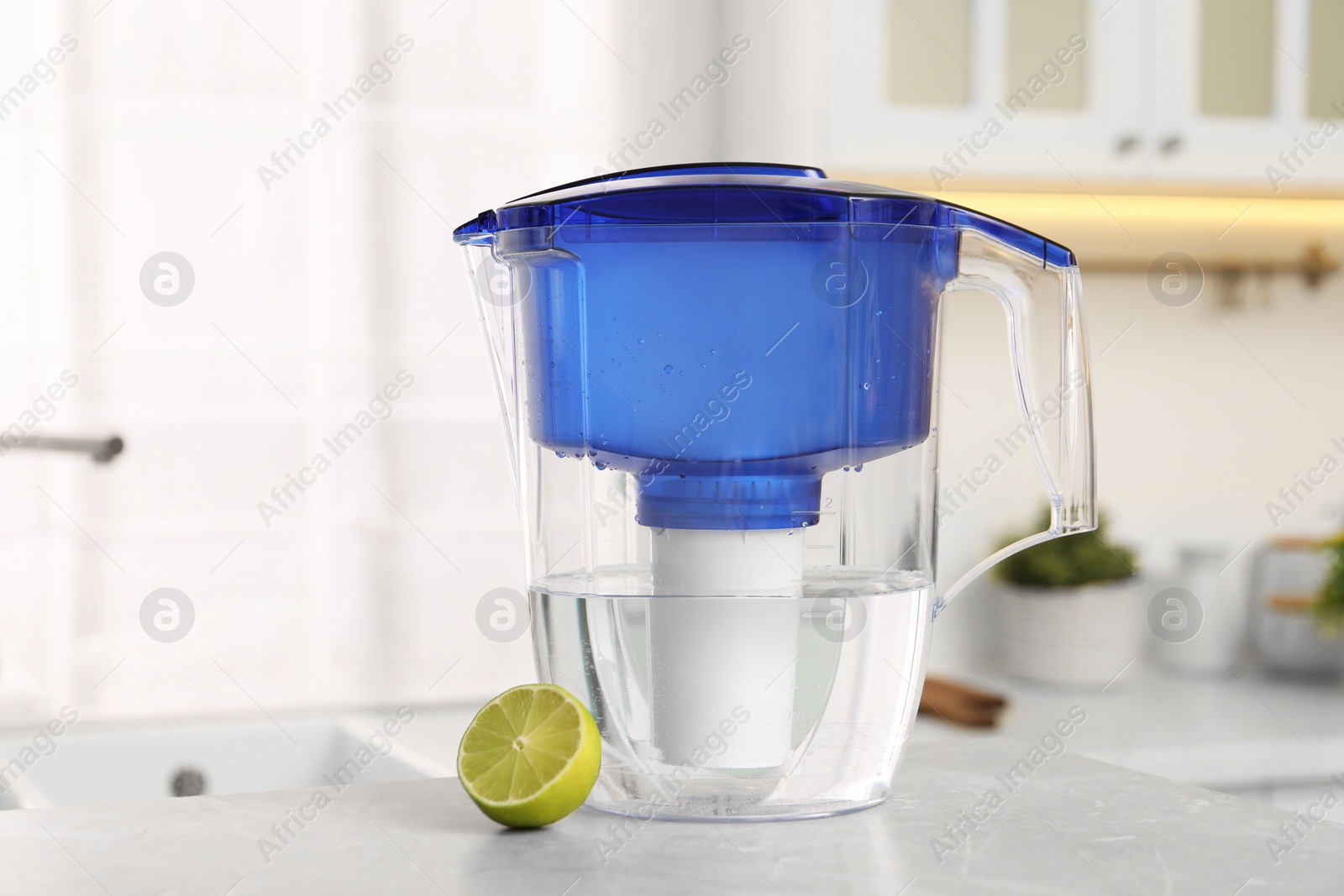 Photo of Water filter jug and lime on light table in kitchen, closeup