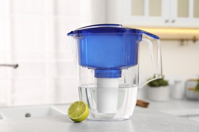 Photo of Water filter jug and lime on light table in kitchen, closeup