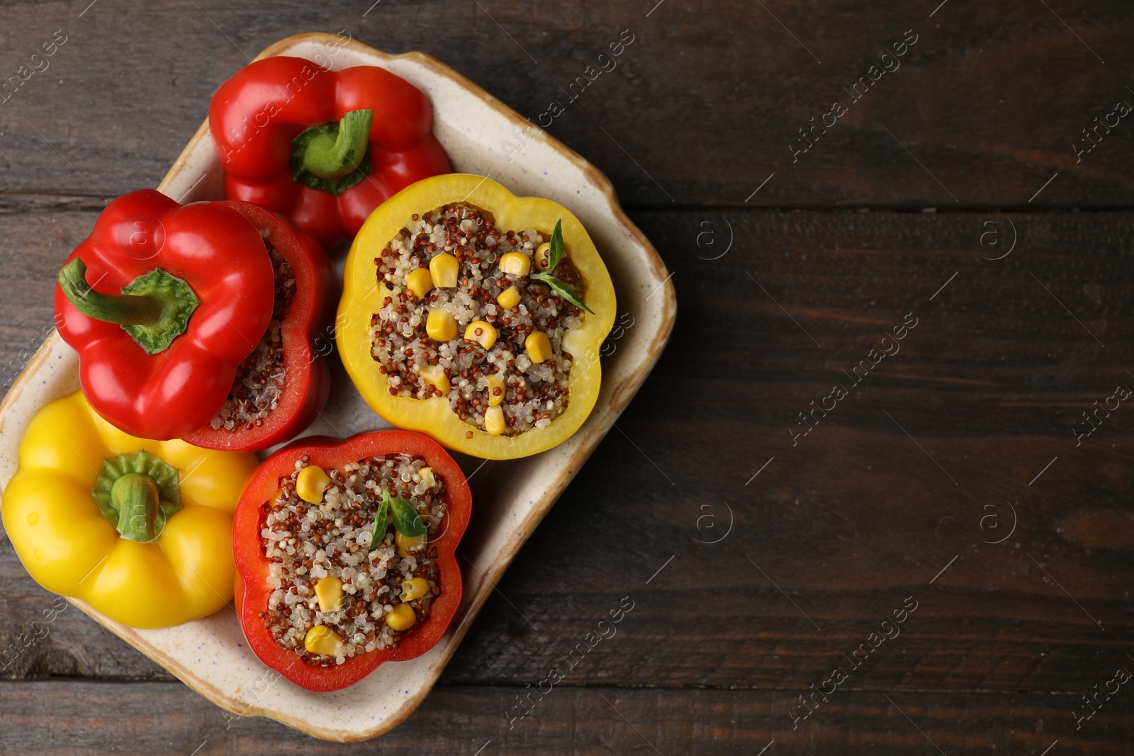 Photo of Quinoa stuffed bell peppers and basil in baking dish on wooden table, top view. Space for text