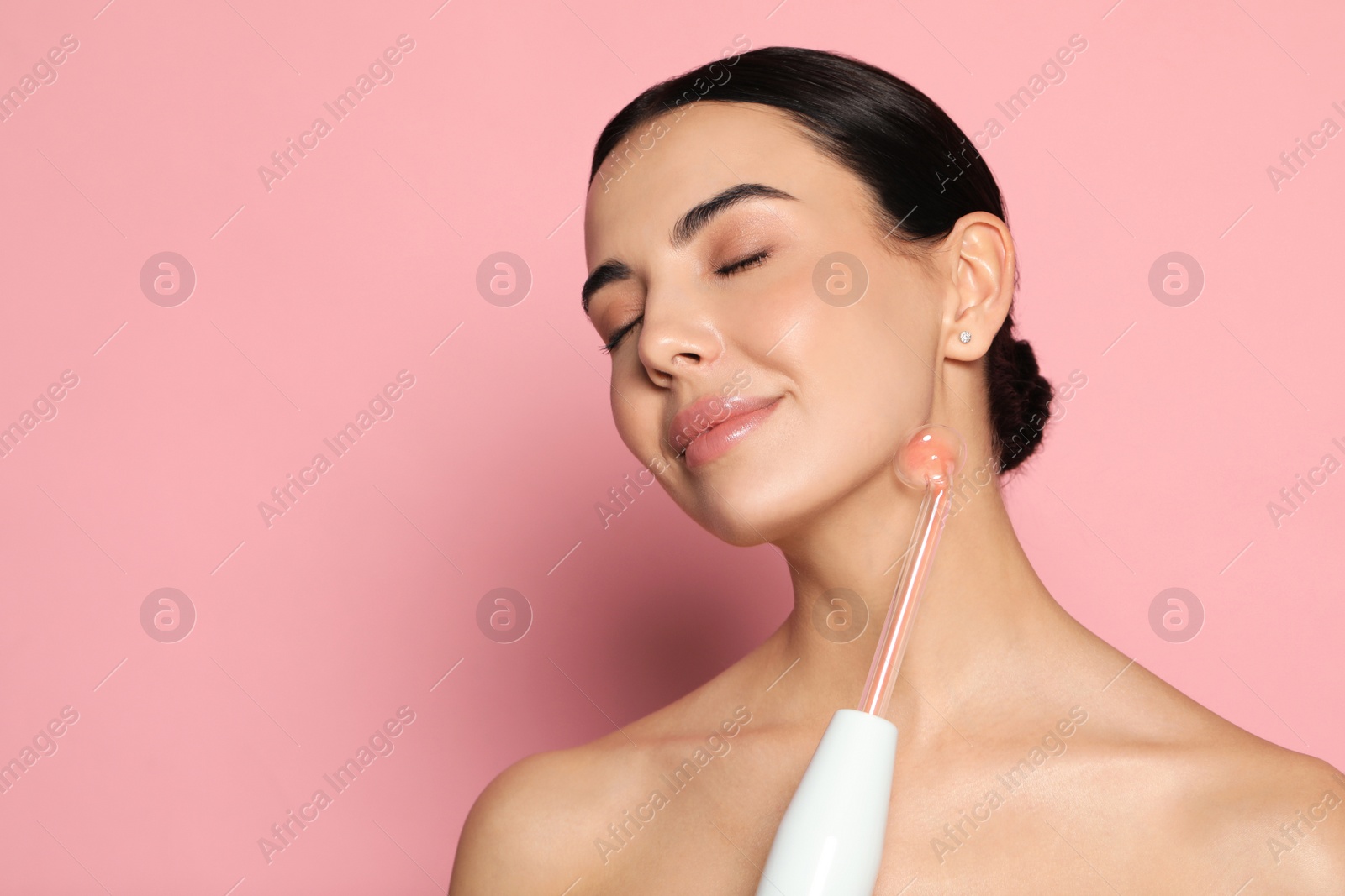 Photo of Woman using high frequency darsonval device on pink background. Space for text