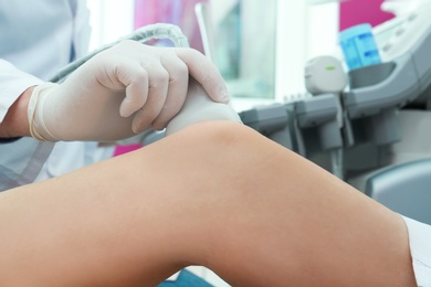 Doctor conducting ultrasound examination of knee joint in clinic, closeup