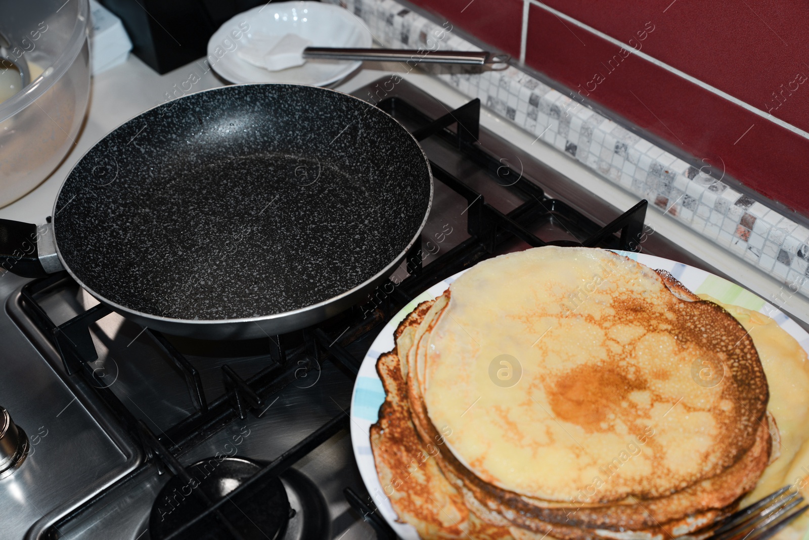 Photo of Plate of freshly made crepes and frying pan on stove in kitchen