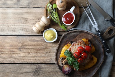 Delicious grilled meat and vegetables served with sauces on wooden table, flat lay. Space for text