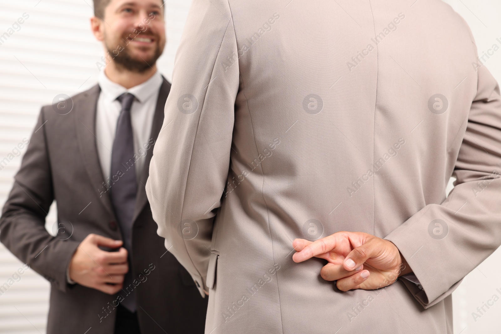 Photo of Employee crossing fingers behind his back while meeting with boss in office, selective focus