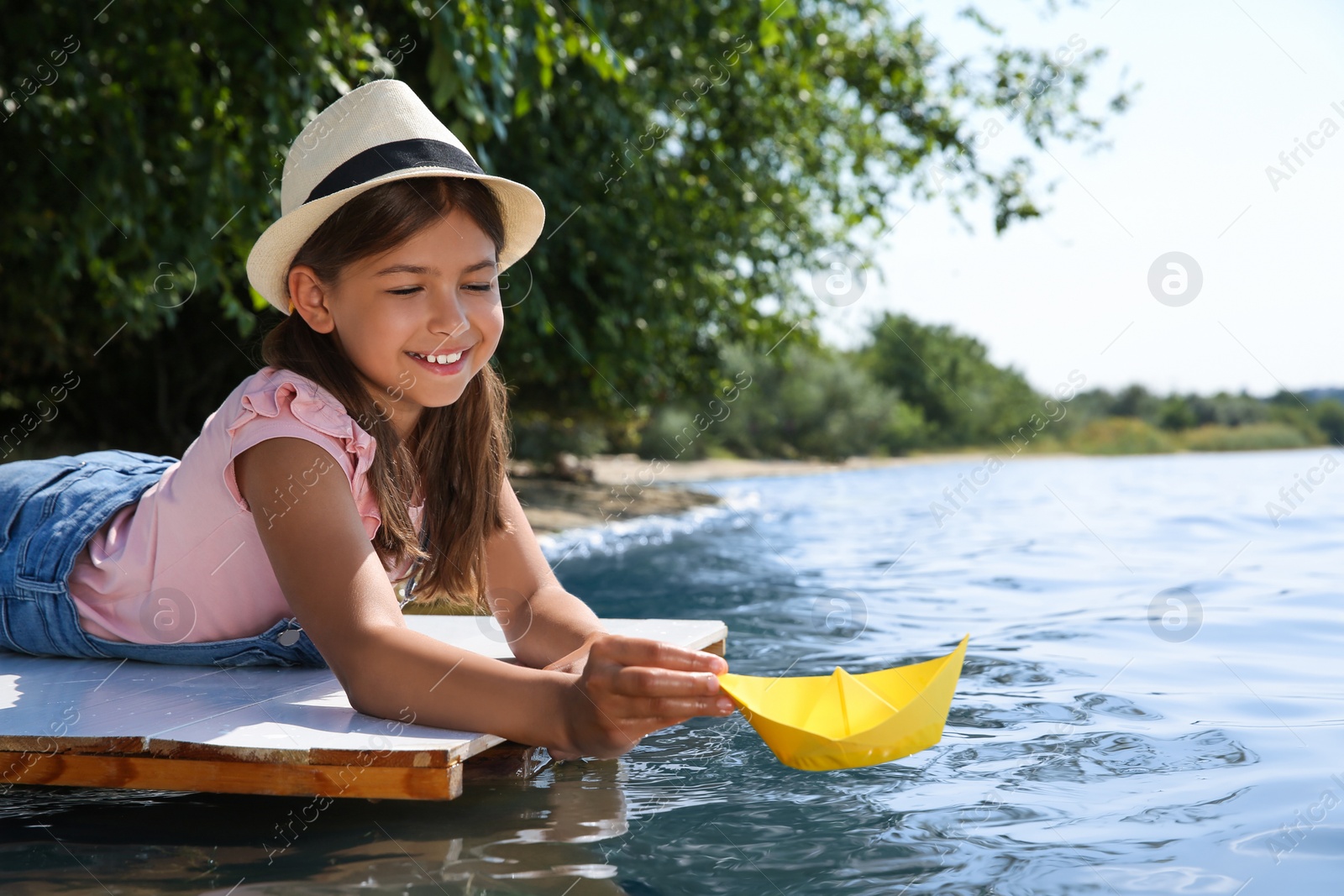 Photo of Cute little girl playing with paper boat on wooden pier near river