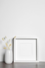 Photo of Empty photo frame and vase with dry decorative spikes on wooden table. Mockup for design