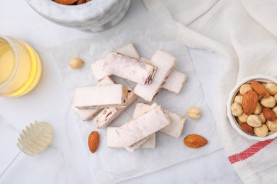Photo of Pieces of delicious nutty nougat, nuts and honey on white table, flat lay