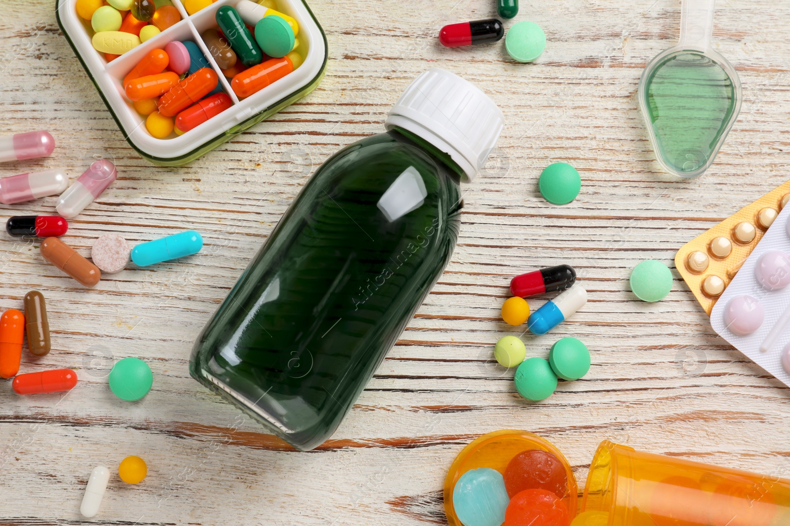 Photo of Flat lay composition with bottle of syrup, dosing spoon and pills on white wooden table. Cold medicine