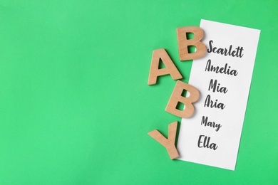 Photo of List of baby names and wooden letters on green background, flat lay. Space for text
