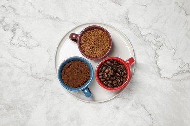 Photo of Instant, ground coffee and roasted beans in cups on white marble table, top view