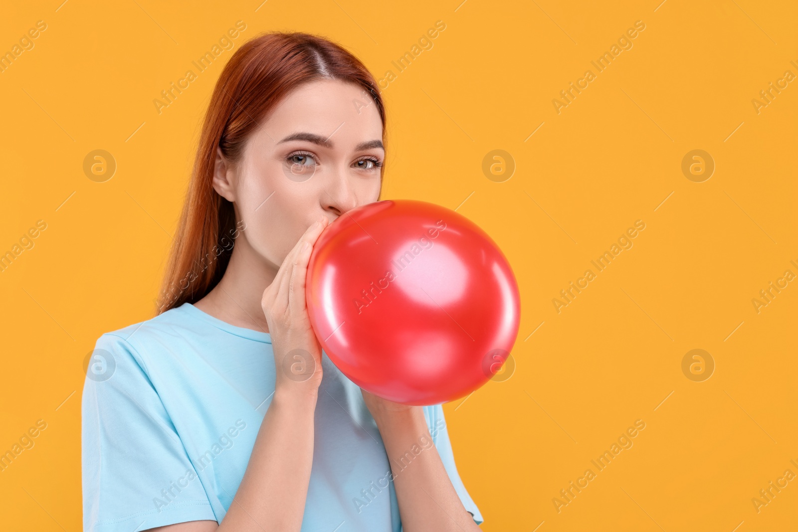 Photo of Woman inflating red balloon on orange background, space for text