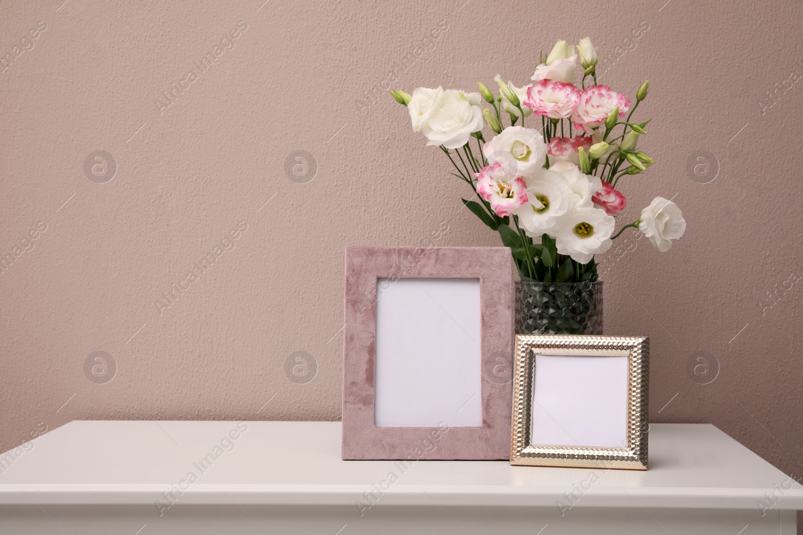 Photo of Empty photo frames and beautiful bouquet on white table near pink wall, space for text