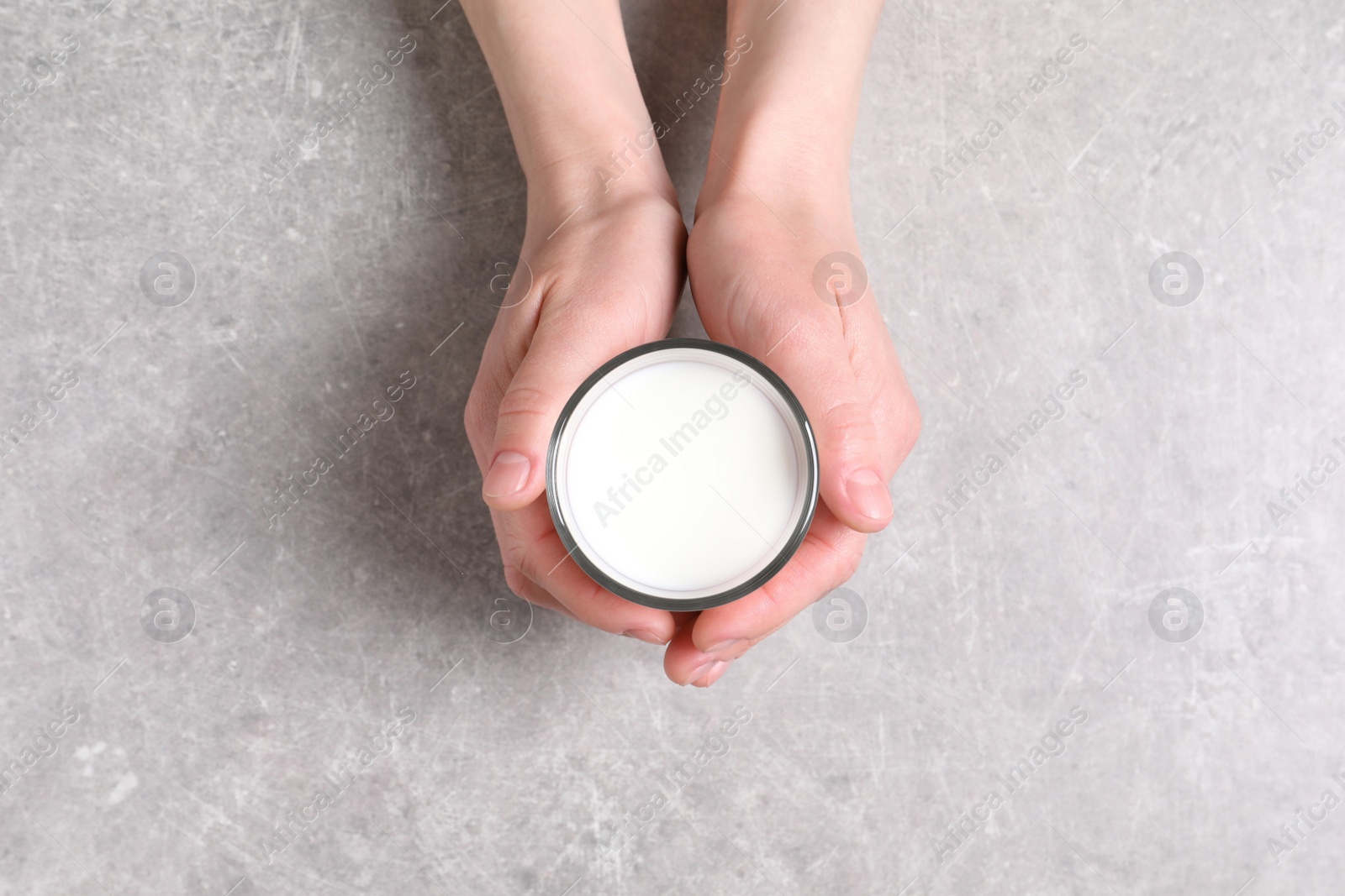 Photo of Woman holding glass of milk at light grey table, top view