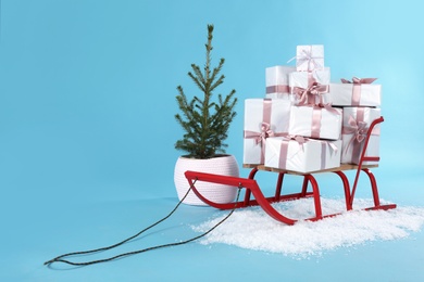 Photo of Sleigh with gift boxes and small fir on light blue background. Space for text