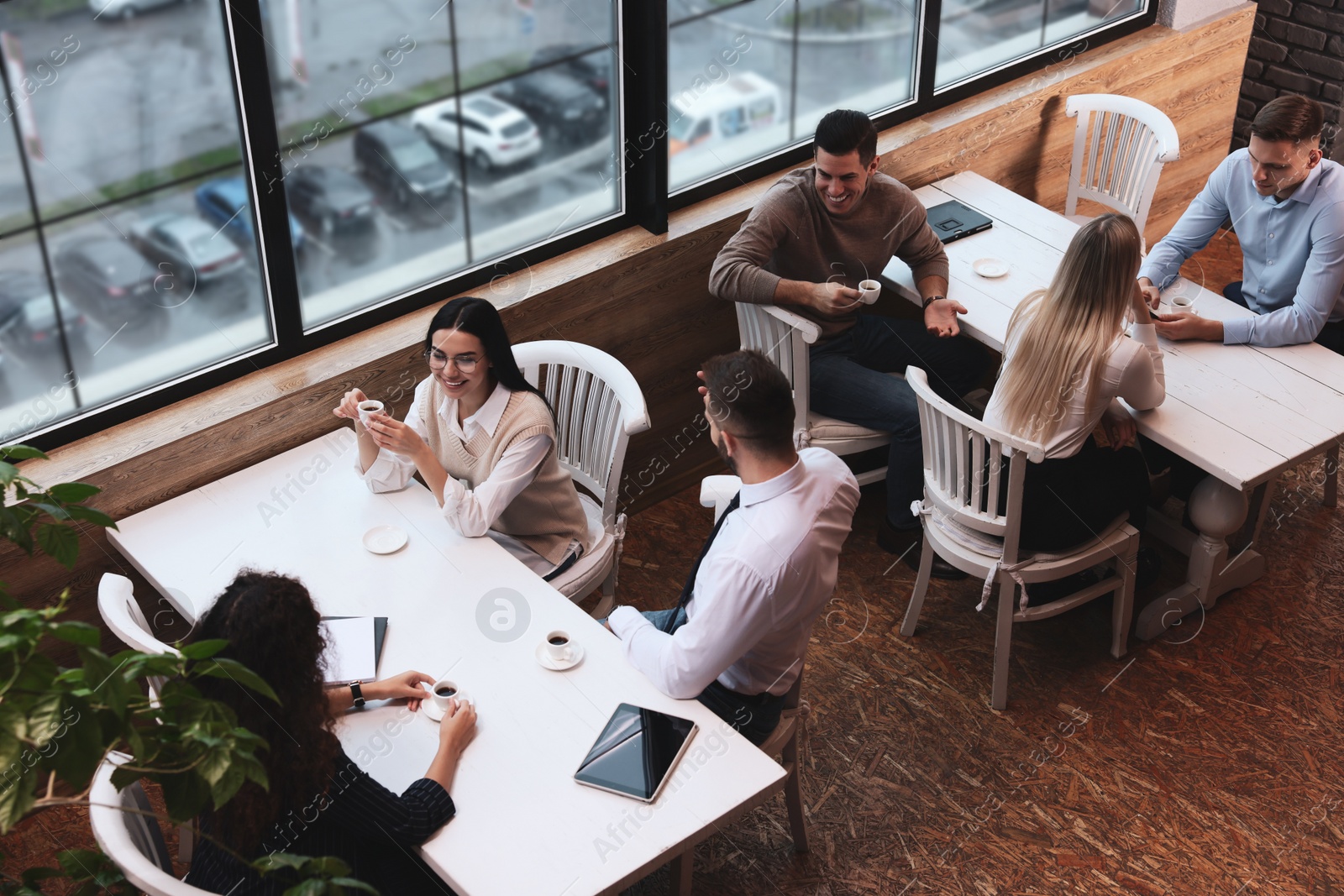 Photo of Coworkers having coffee break near window in cafe, above view